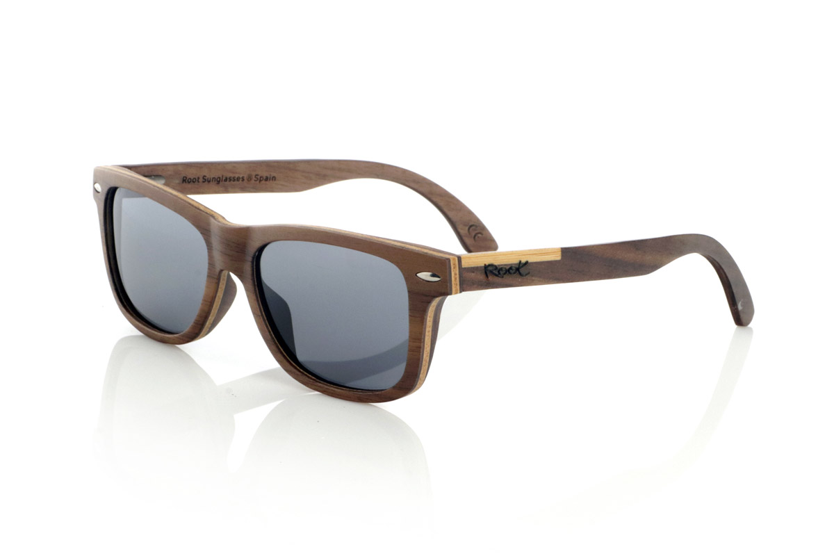 Wood eyewear of Walnut WOODSUNSET SK. The Woodsunset wooden sunglasses are made from black walnut wood, offering an elegant and timeless design with a natural finish. Its laminated structure includes a natural maple interlayer, providing a subtle contrast that enhances its sophistication.

The temples feature a unique detail with a combination of walnut and oak, giving this model a distinctive touch. In addition, the front features small metal ornaments, which not only reinforce the structure, but also add a vintage feel to its design.

Thanks to its classic and versatile shape, the Woodsunset are an excellent choice for both men and women looking for wooden glasses with character and style.

Measurements: 147x47 Caliber: 49 for Wholesale & Retail | Root Sunglasses® 