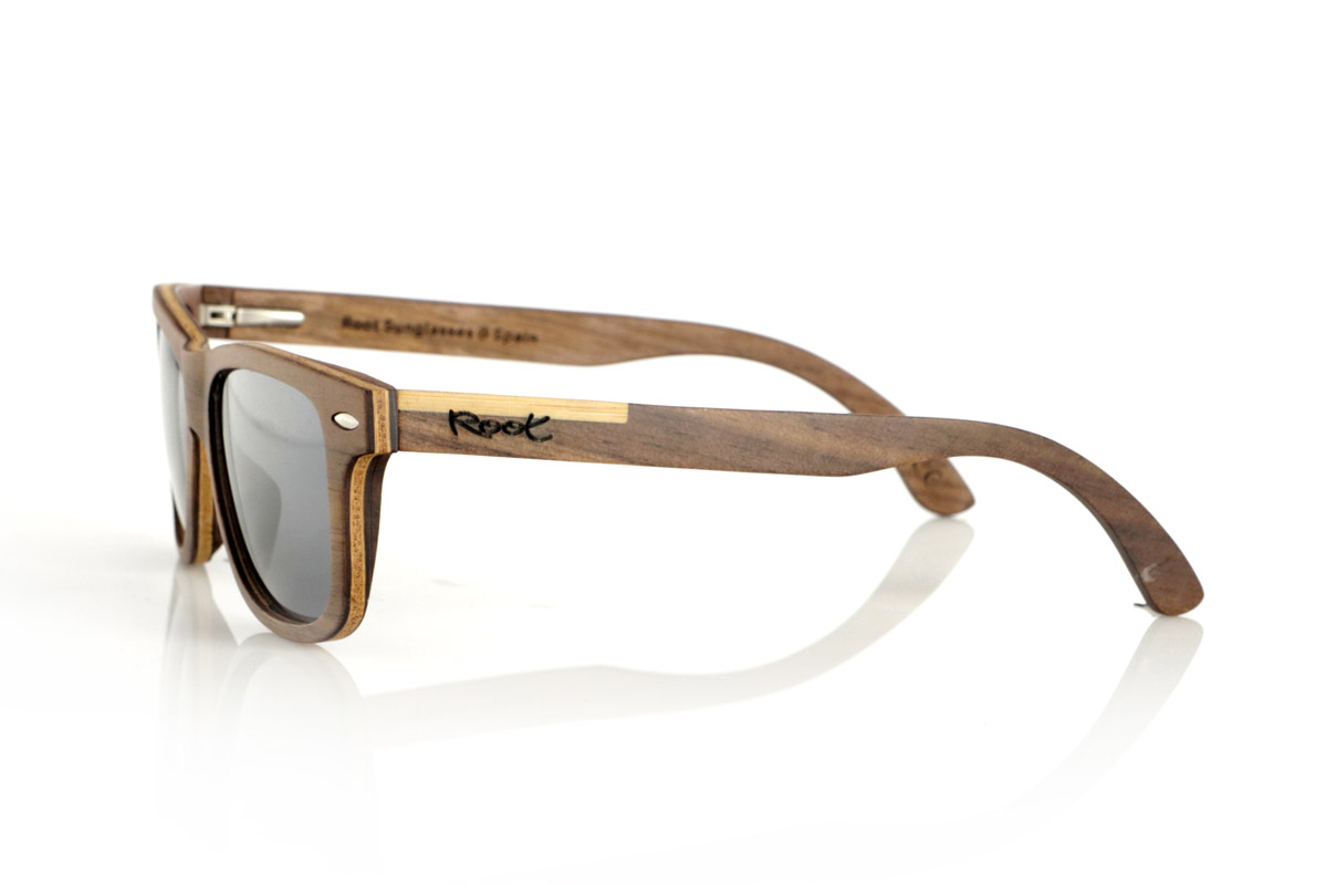 Wood eyewear of Walnut WOODSUNSET SK. The Woodsunset wooden sunglasses are made from black walnut wood, offering an elegant and timeless design with a natural finish. Its laminated structure includes a natural maple interlayer, providing a subtle contrast that enhances its sophistication.

The temples feature a unique detail with a combination of walnut and oak, giving this model a distinctive touch. In addition, the front features small metal ornaments, which not only reinforce the structure, but also add a vintage feel to its design.

Thanks to its classic and versatile shape, the Woodsunset are an excellent choice for both men and women looking for wooden glasses with character and style.

Measurements: 147x47 Caliber: 49 for Wholesale & Retail | Root Sunglasses® 